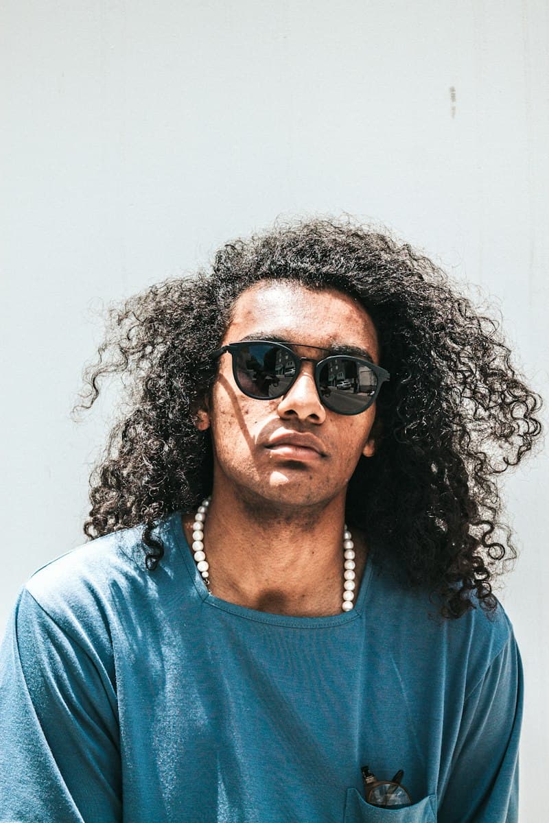 Person with long curly hair wearing round black sunglasses